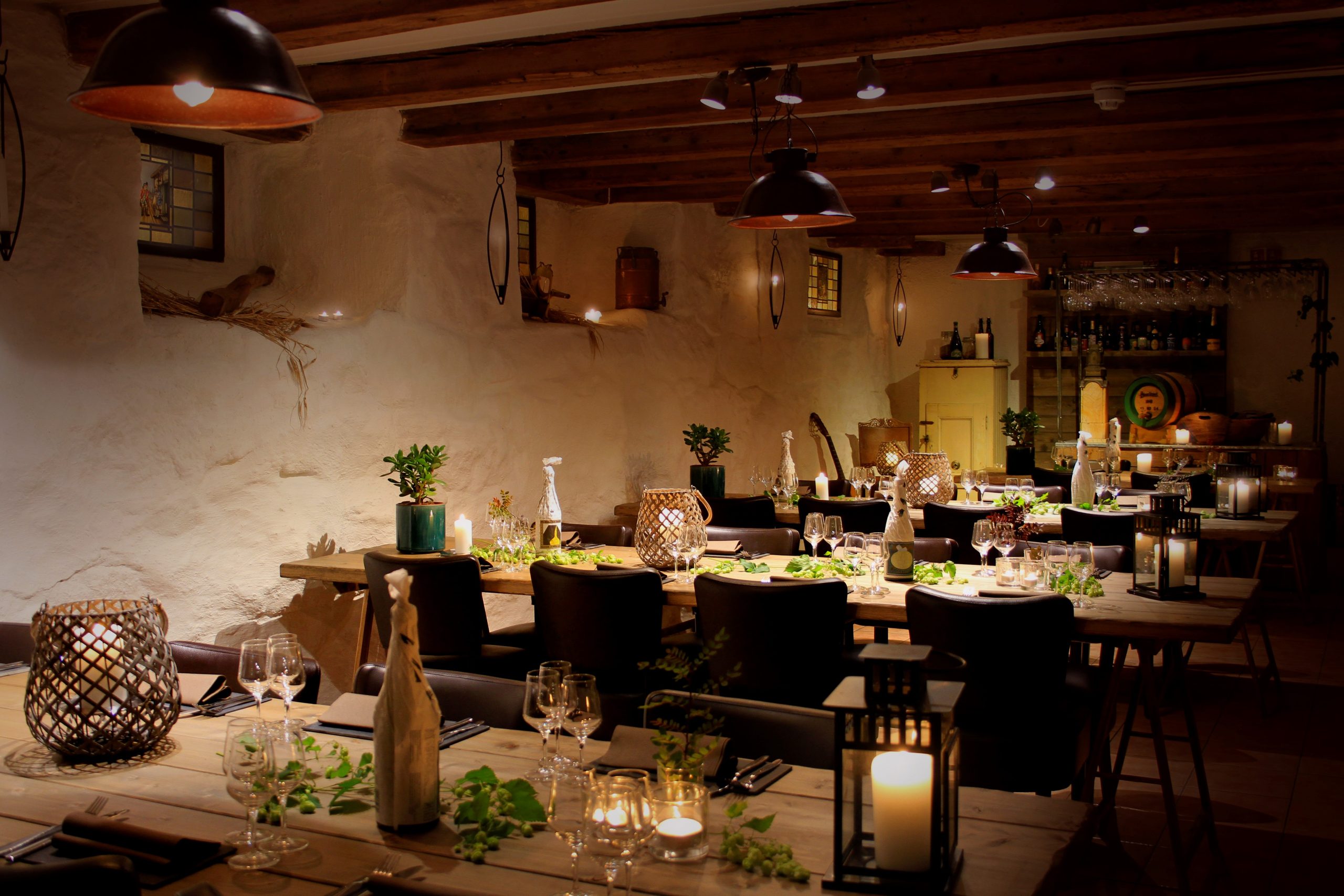 Rustic dining room with long wooden tables, candlelight, and greenery for a dinner event in a warmly lit space.