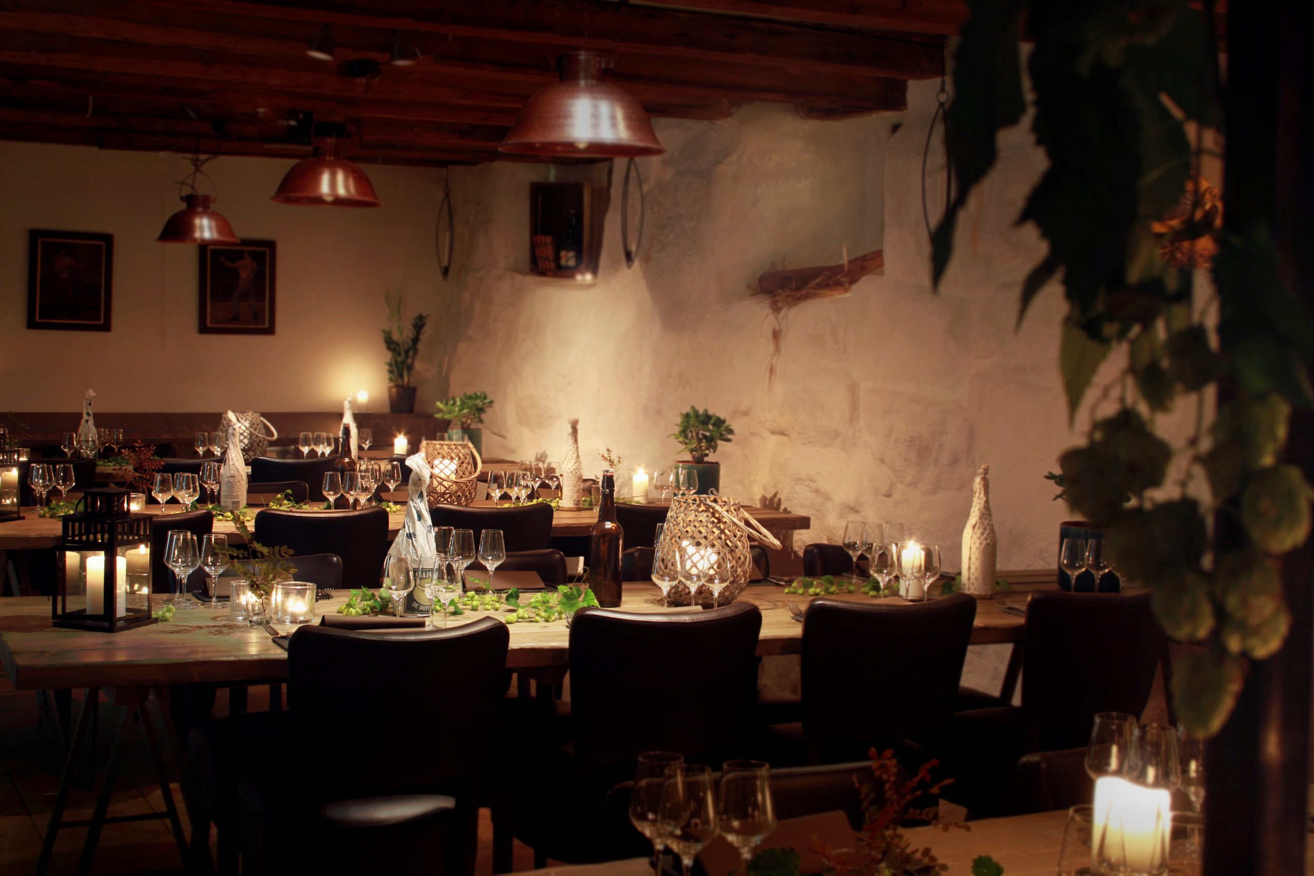 Rustic candlelit dinner setup in a warmly lit dining room with copper lamps and vines on the tables.