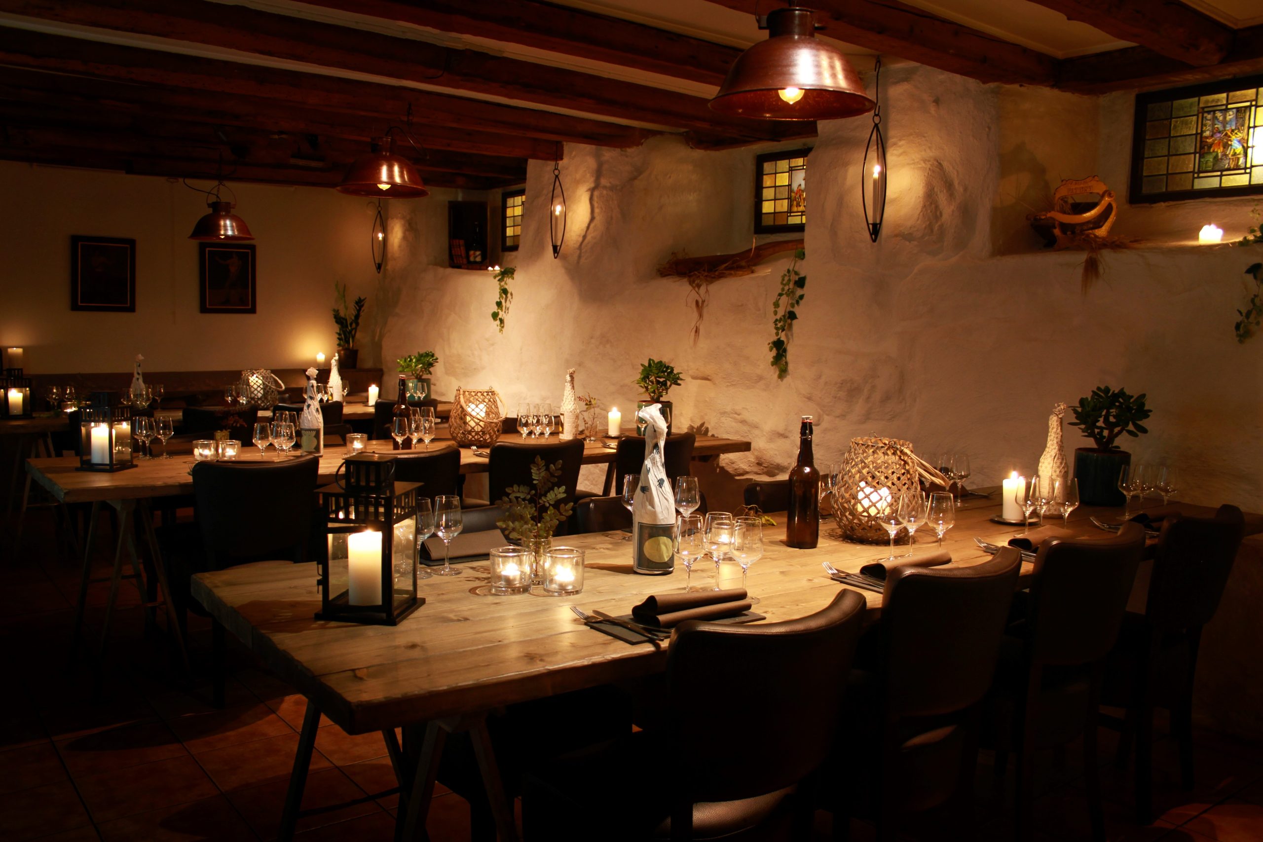 Cozy dimly lit restaurant with wooden tables, candles, and wine glasses arranged for a dinner service