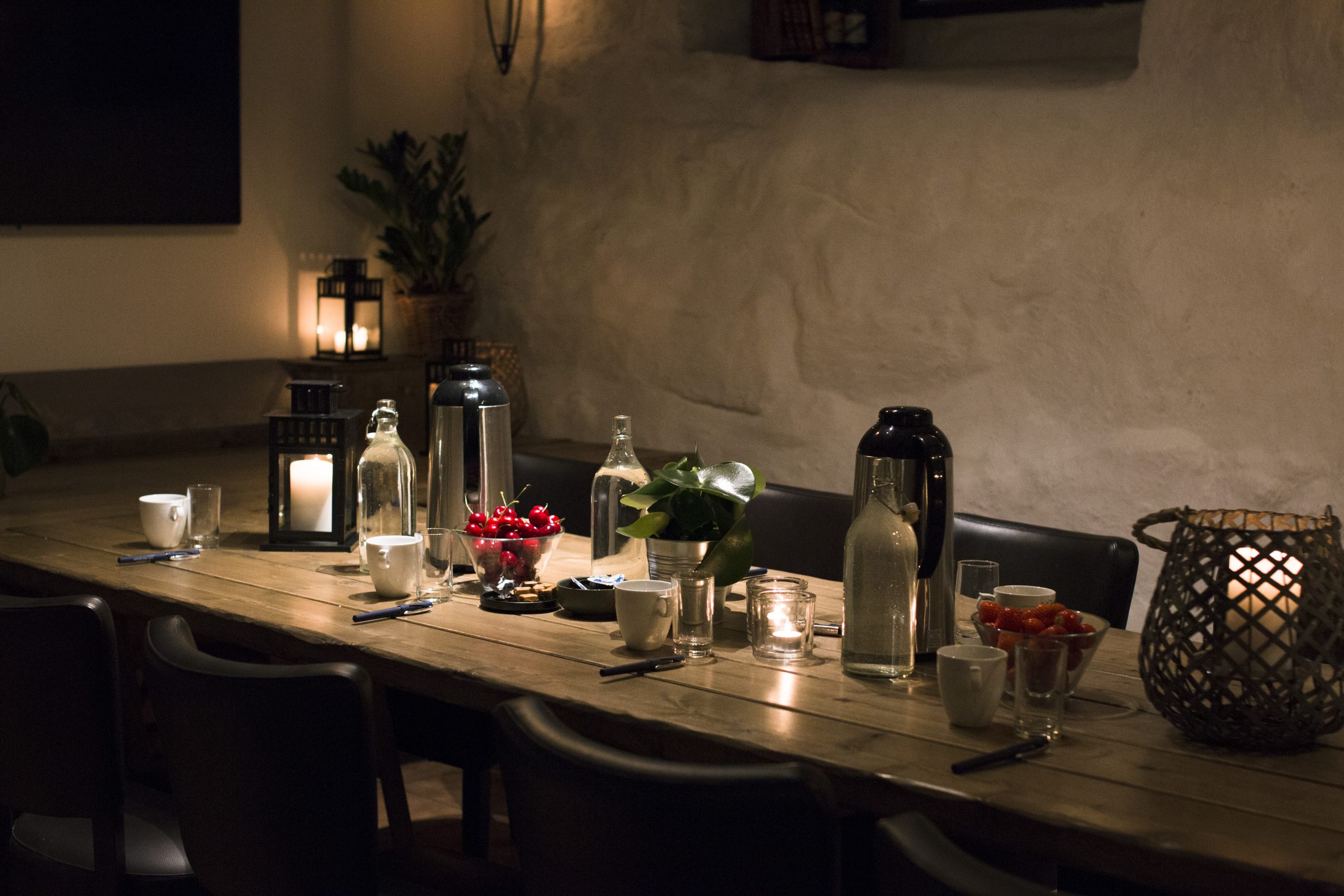 Dimly lit dining table set with candles, glass bottles, and a bowl of cherries for a cozy meal.
