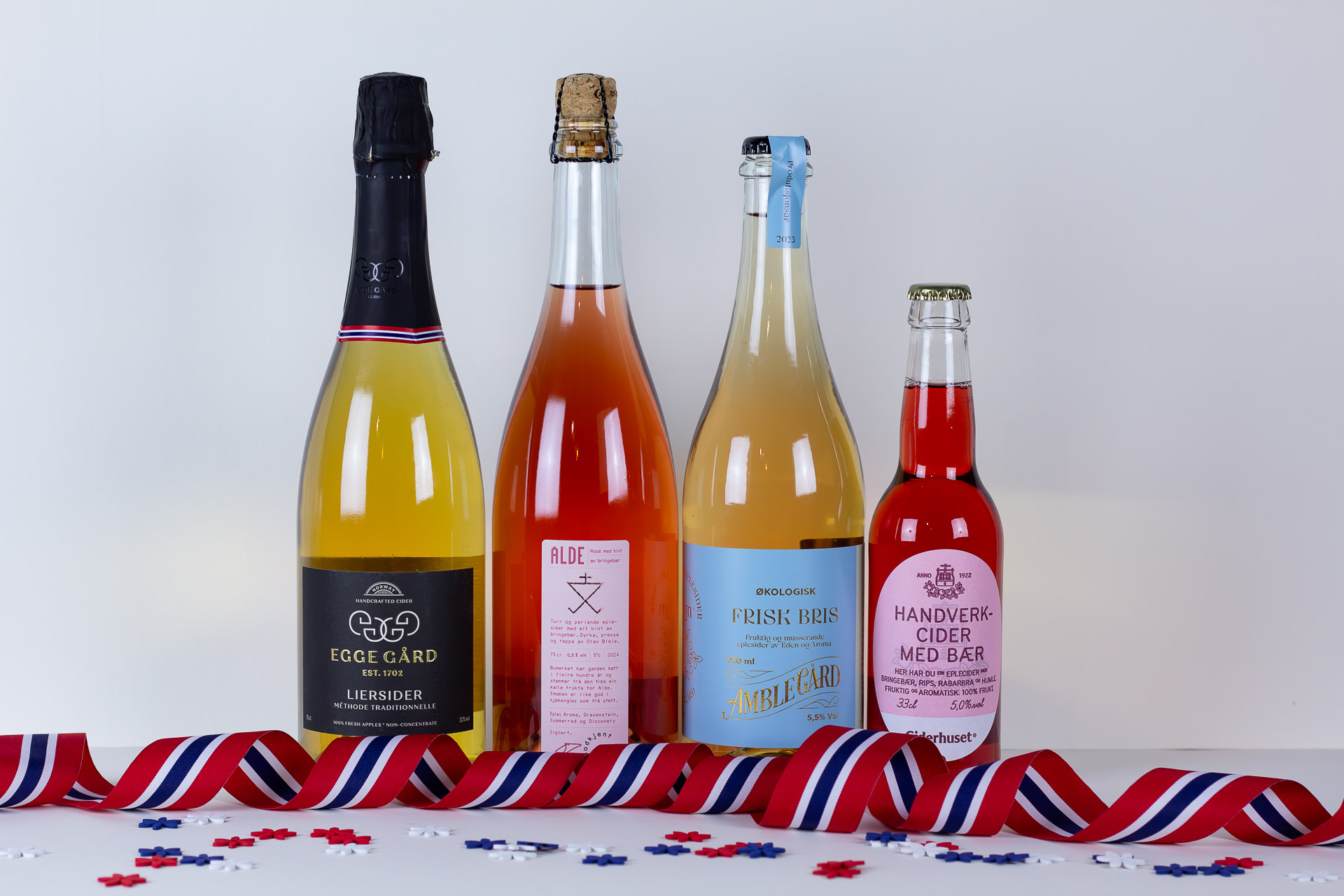 Four bottles of sparkling beverages lined up on a white surface with redwhiteblue ribbons and scattered confetti at their base