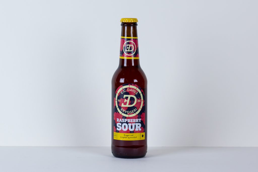 Brown glass beer bottle with a yellow cap standing upright on a white surface label reads Raspberry Sour and features redpink graphics around a circular logo