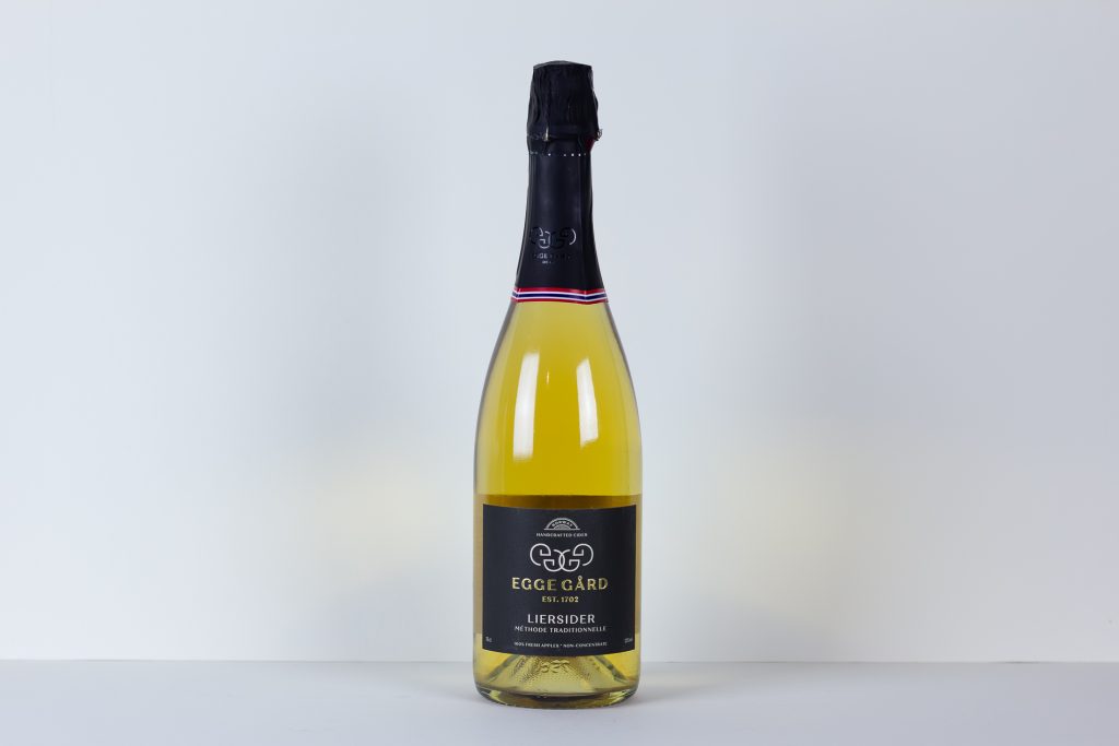 Bottle of Eggegård cider on a white surface with a dark foil top and label facing forward