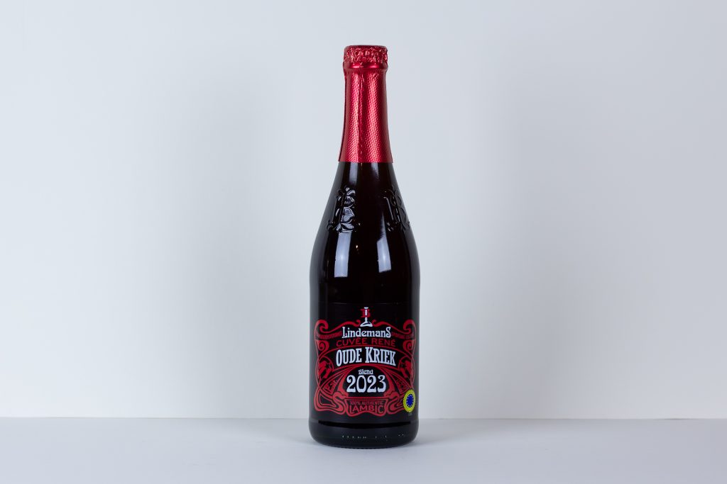 Bottle of Lindemans Oude Kriek Lambic with red foil cap and ornate red label 2023 blend on a white surface