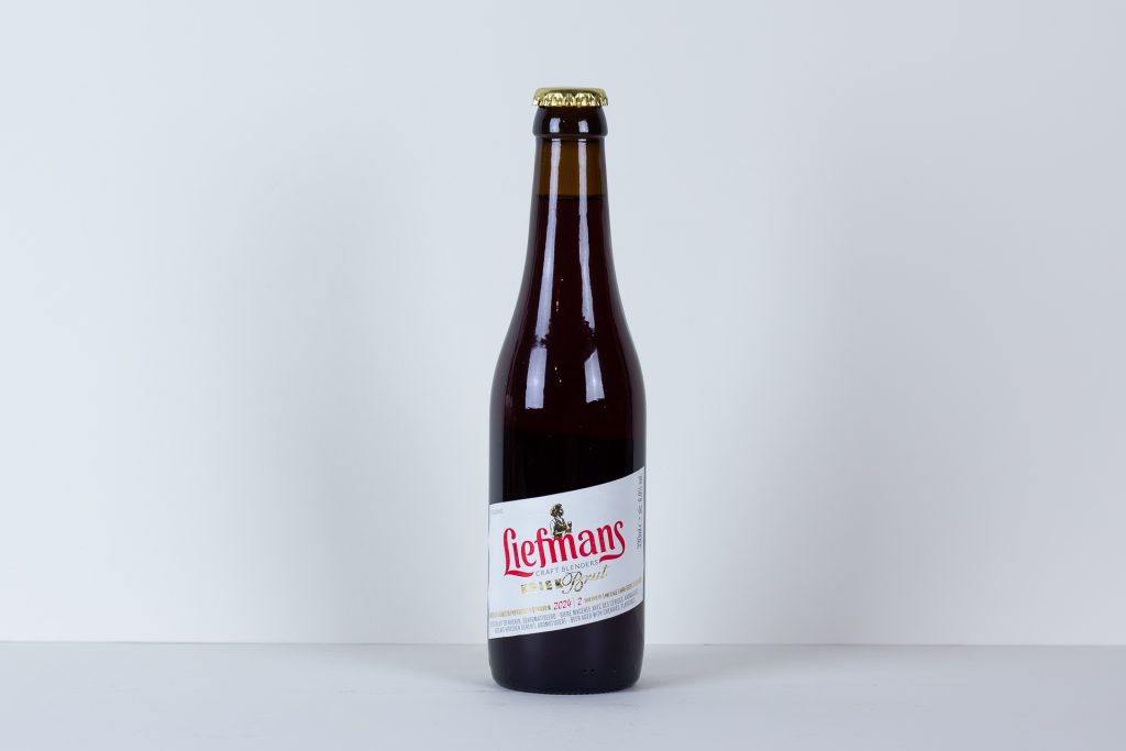 Single brown beer bottle with a white label reading Liefmans on a pale white background surface and backdrop