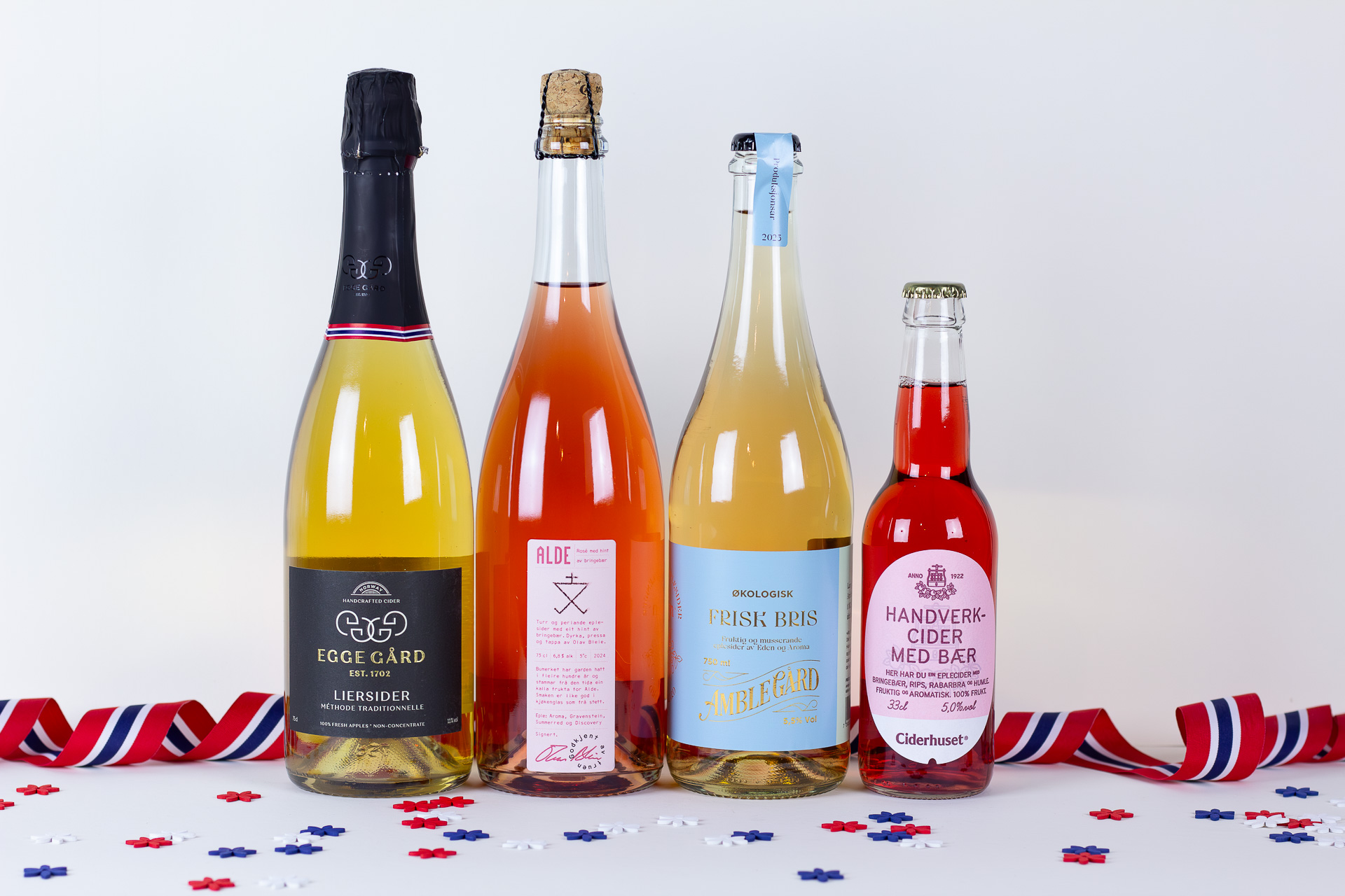Row of four glass bottles with corks on a white surface surrounded by red white and blue confetti ribbons for a festive scene