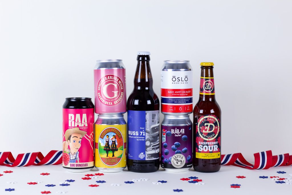 Assorted beer cans and bottles lined up on a white surface with red, white, and blue streamers in the background/foreground.